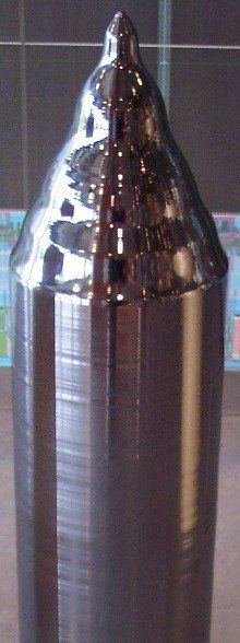 A metal object with a cone shaped top is sitting on a table.