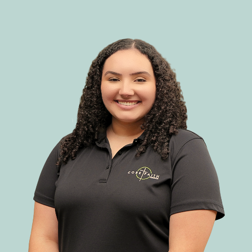 Woman with curly dark hair smiles, looking over her shoulder at the camera, wearing a red shirt, outdoor setting.
