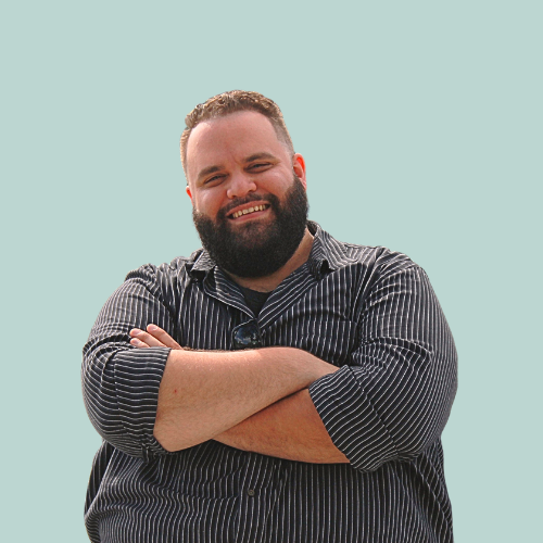 Man in striped shirt smiles, standing in a recording studio with soundproofing.