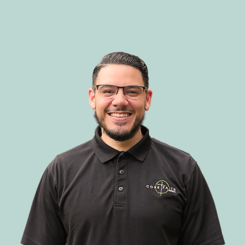 Man sitting on a park bench, wearing glasses and a blue polo shirt, resting arm on bench, looking toward the camera.