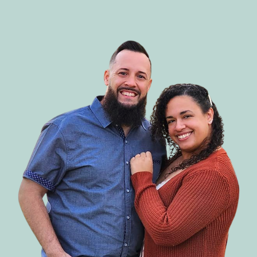 Two smiling people, a man with a beard and a woman with glasses, sitting at a table.
