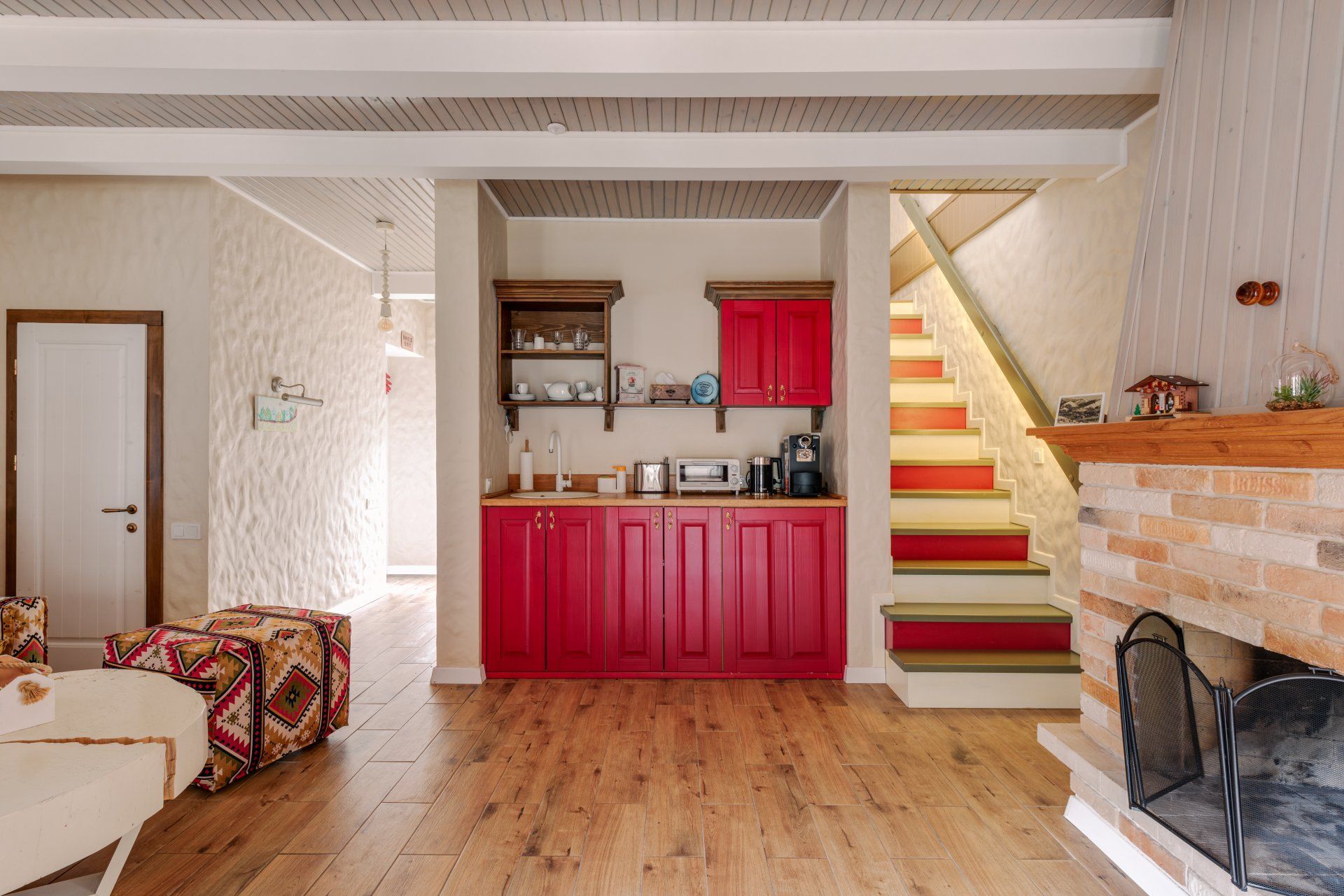 A living room with red cabinets , laminate flooring and stairs leading up to the second floor.