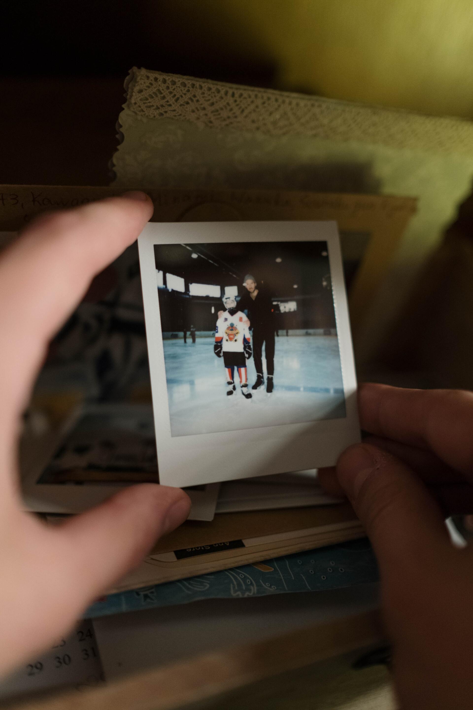 Person holding an old photo of a father-and-son moment on a hockey game.