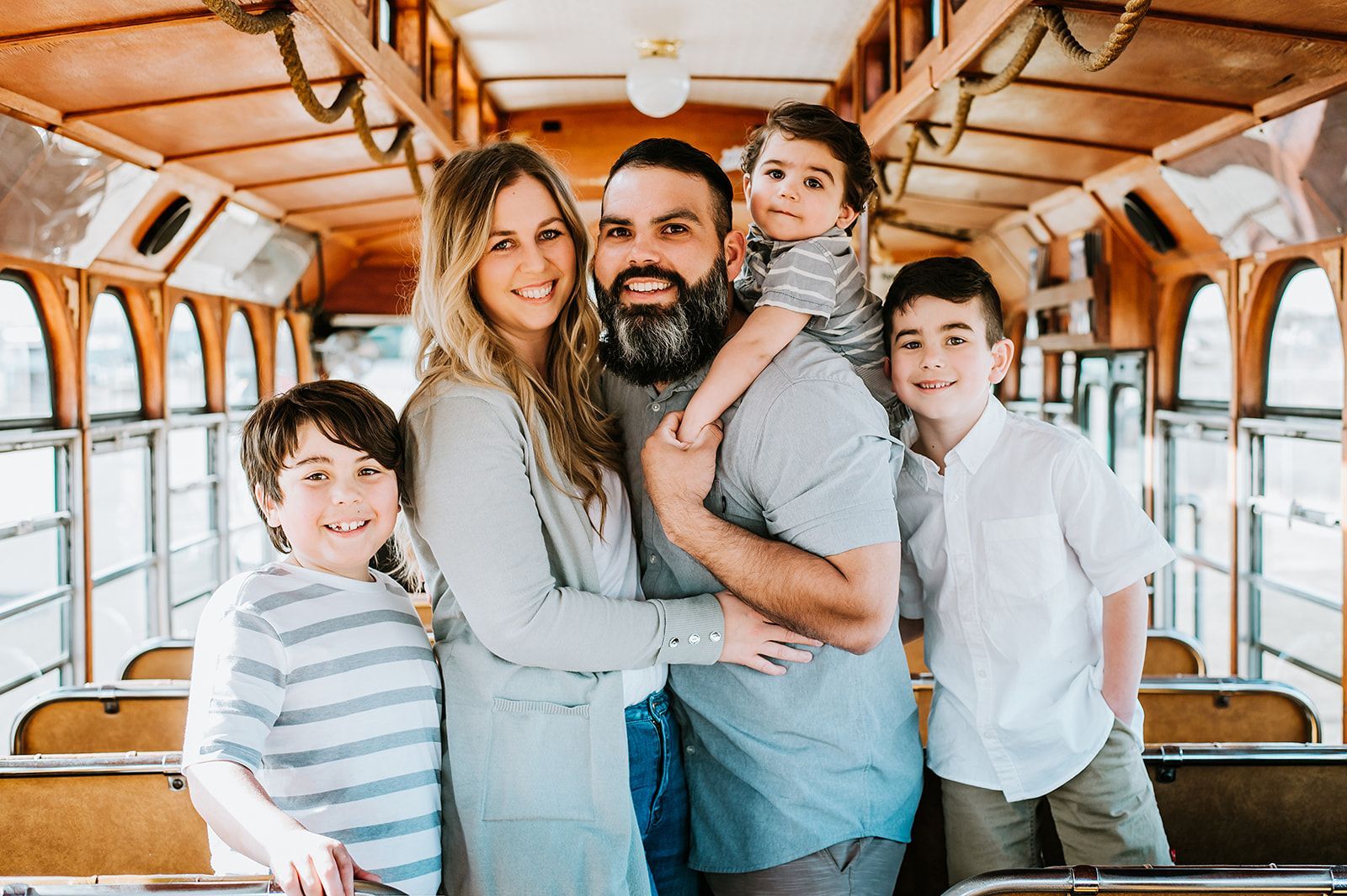 A smiling family of five poses together inside a classic wooden trolley car with rows of seats.