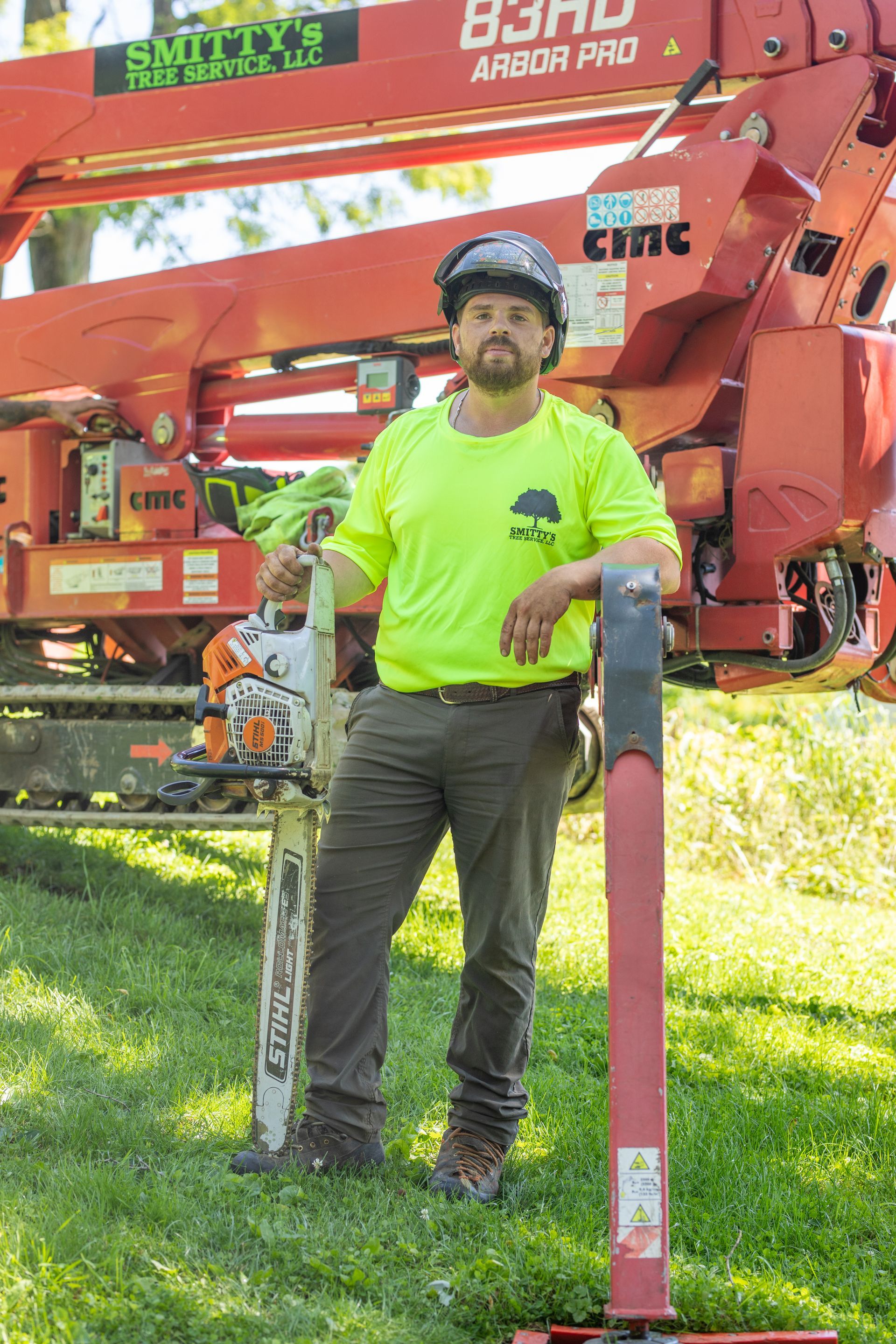 Man in neon shirt, holding chainsaw, leaning on pole, by tree lift truck.