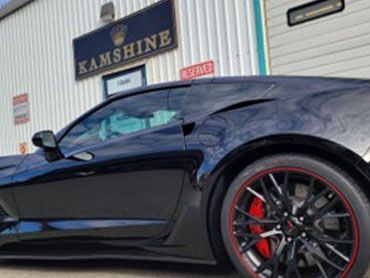 Black Corvette with red-trimmed wheels parked outside a business called Kamshine.