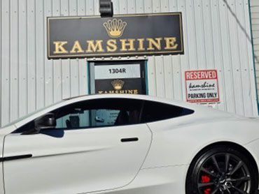 White sports car parked in front of Kamshine business sign.