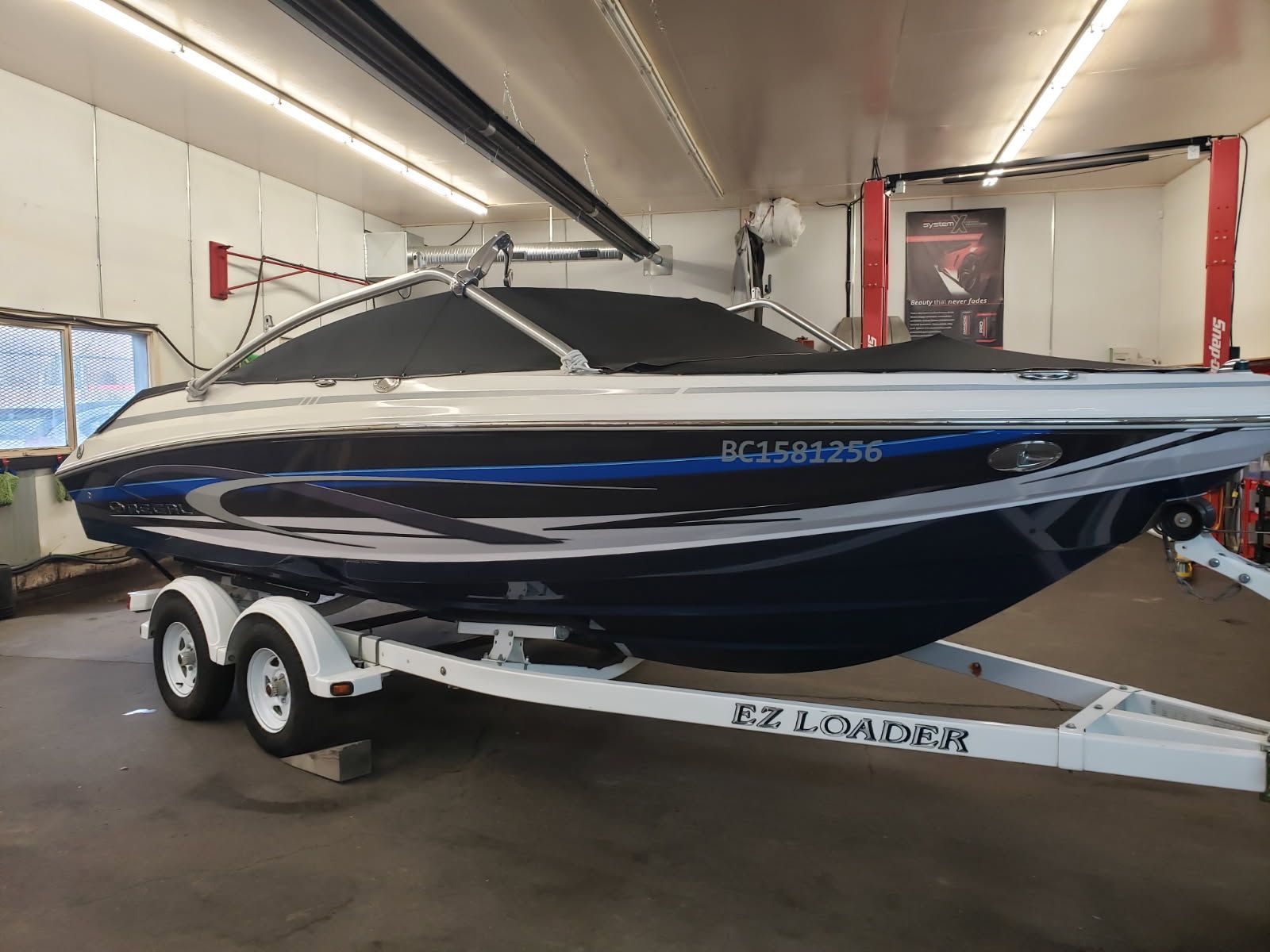A white and blue boat on a white EZ Loader trailer inside a garage.