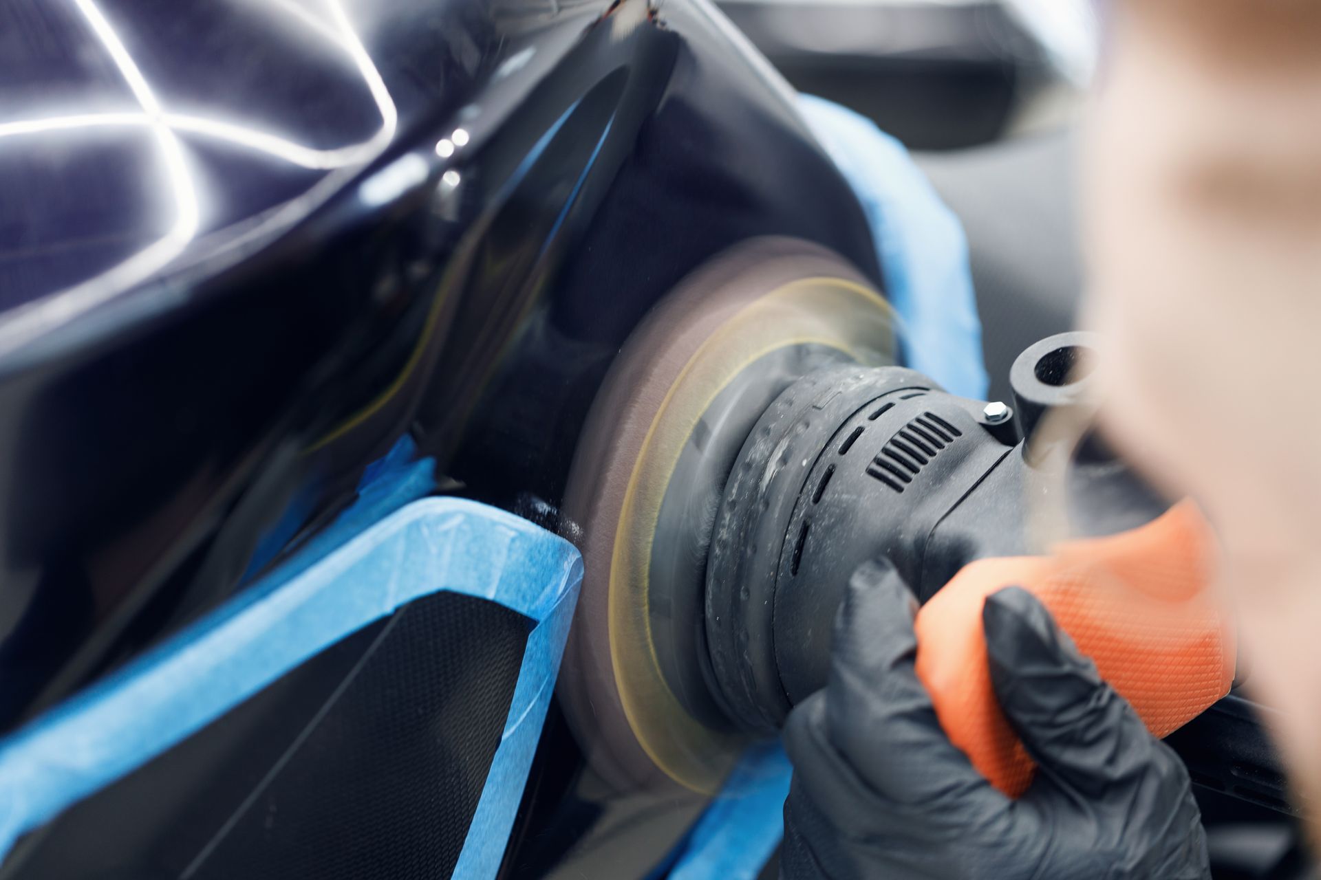 Gloved hand applying ceramic coating to a dark gray car's fender.