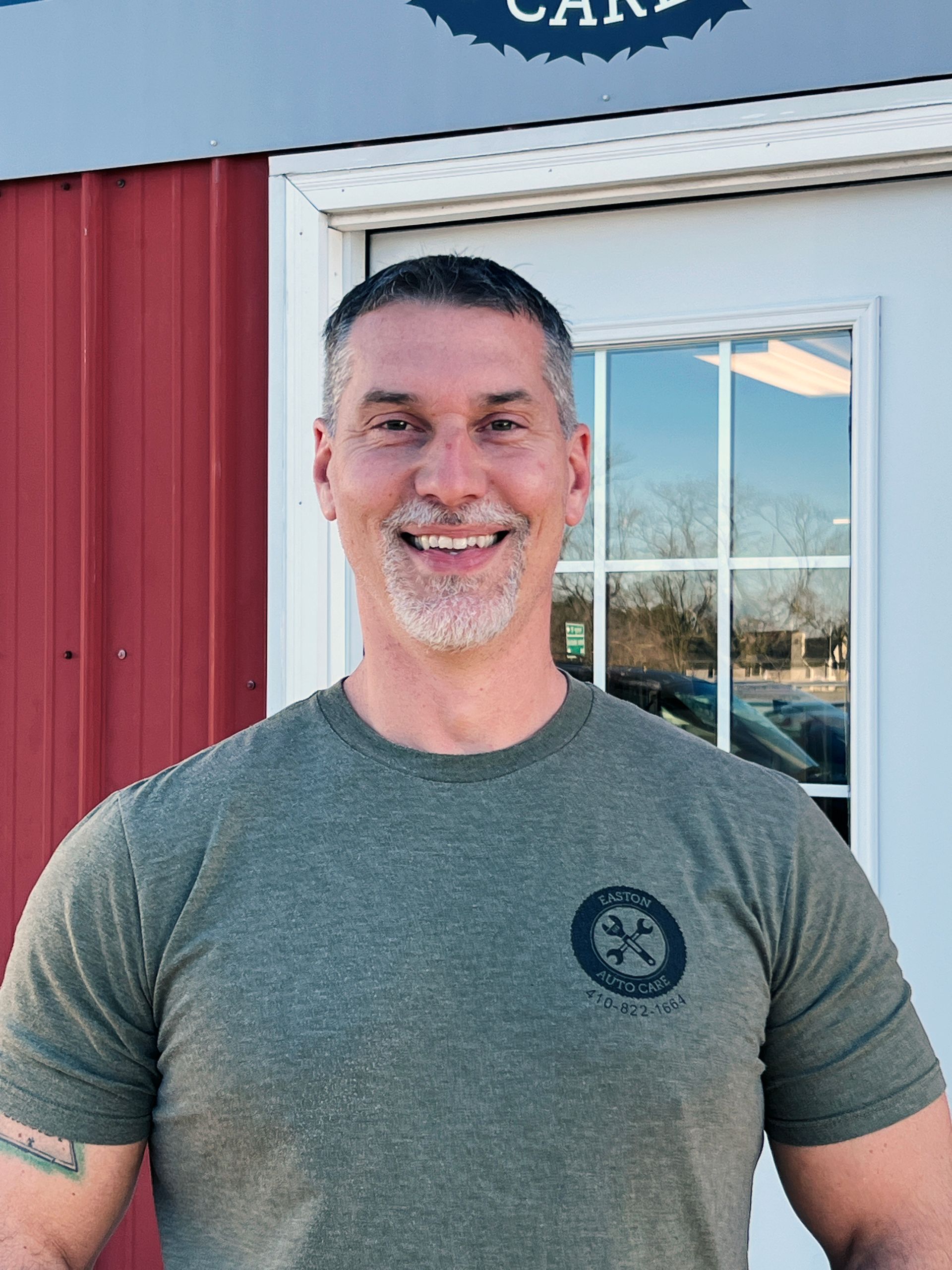 A man in a green shirt is smiling in front of a red building.