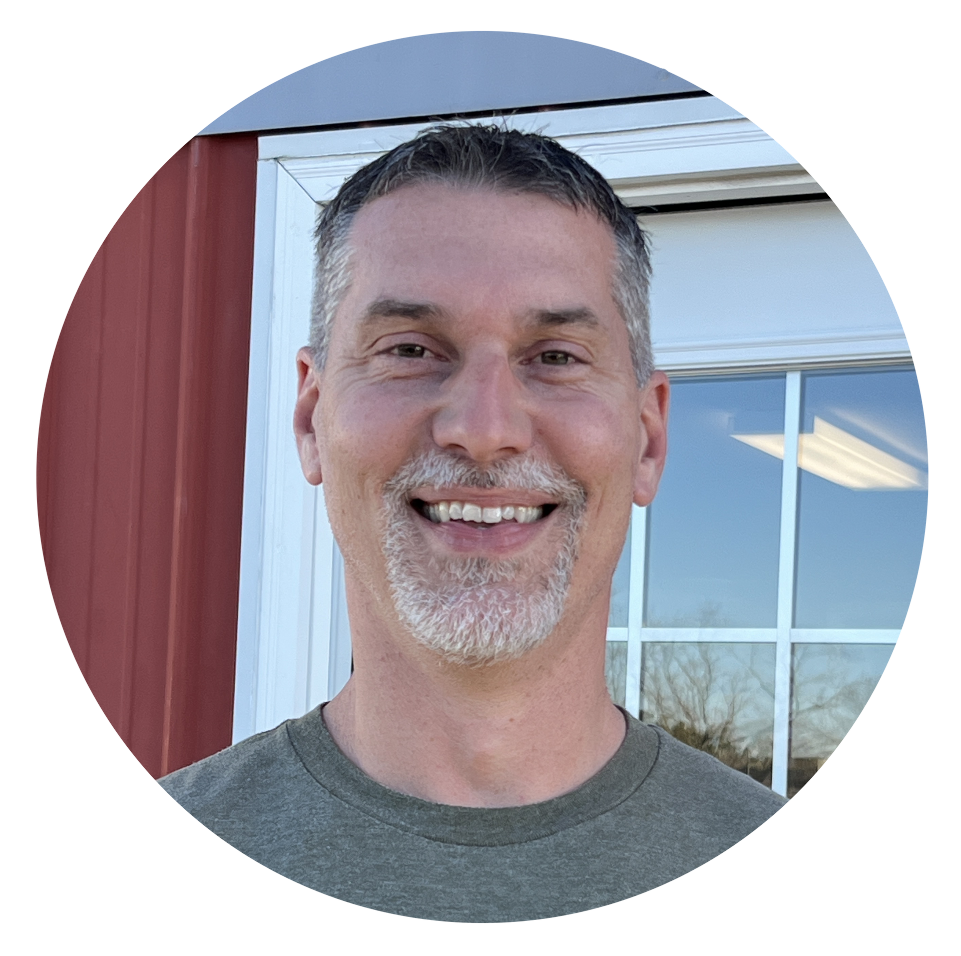 A man with a beard is smiling in front of a window