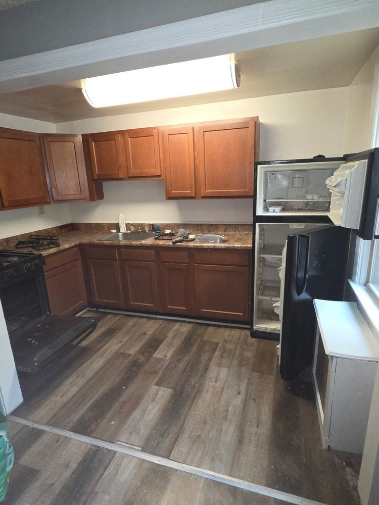 Kitchen with brown cabinets, stove, refrigerator, and wood-look flooring.