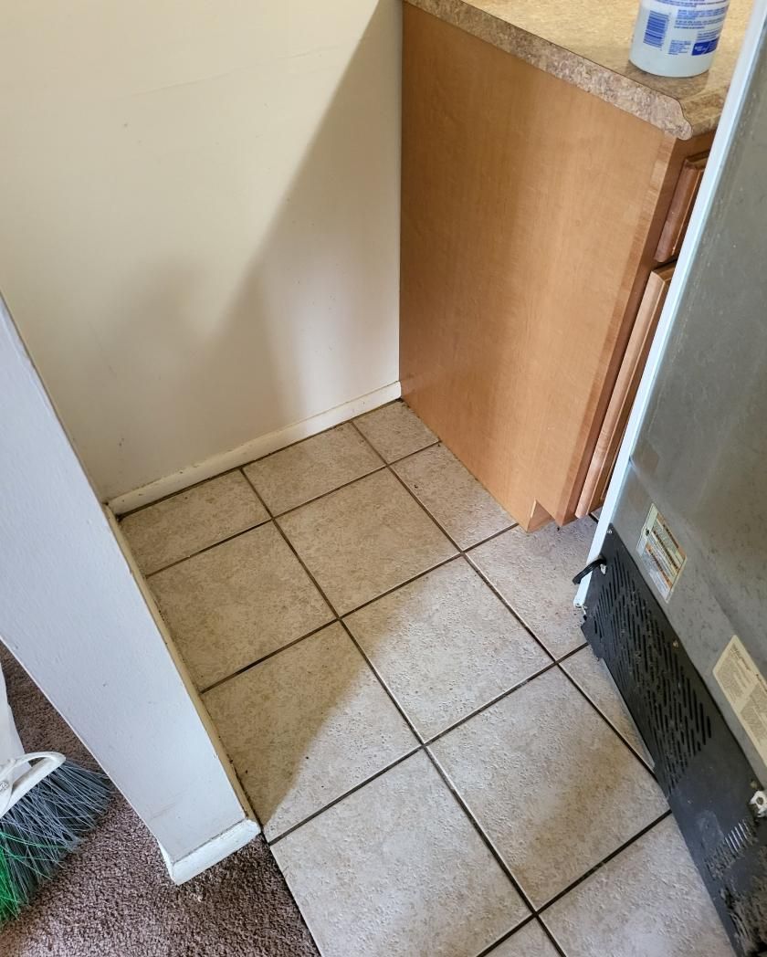 Tiled kitchen floor beside a cabinet and wall; a broom is in the lower left corner and a refrigerator is on the right.
