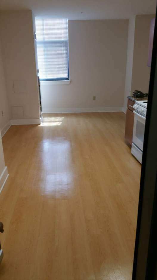 Empty apartment with hardwood floors, a window, and a kitchen appliance.