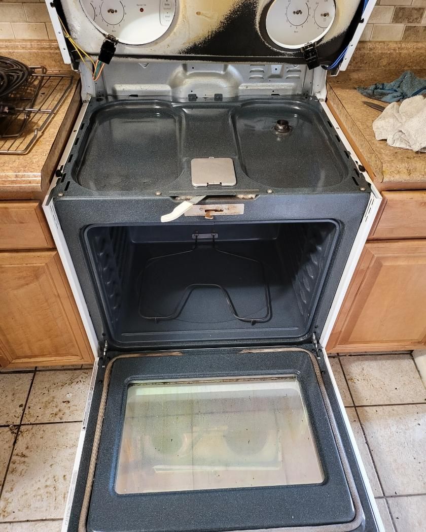 Open white oven with burners and interior visible. Dirty oven door open. Countertop in background.