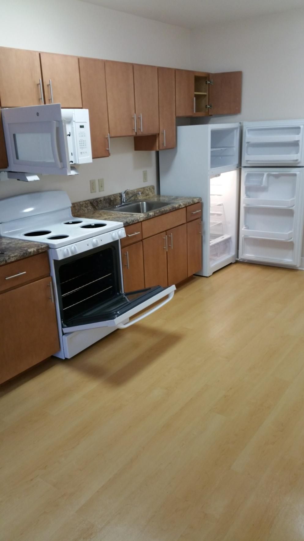 Kitchen with white appliances, wooden cabinets, and a light wood floor. The oven and fridge doors are open.