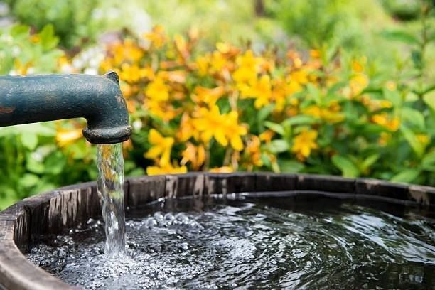 Water is coming out of a faucet into a wooden barrel.