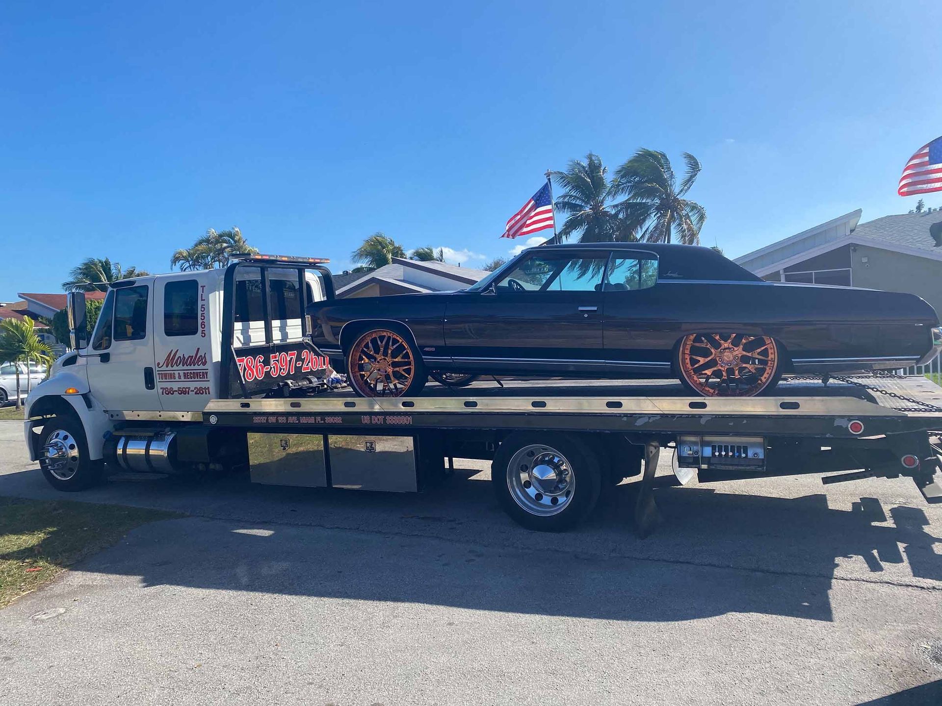 Black classic car with copper rims on a tow truck, outdoors.