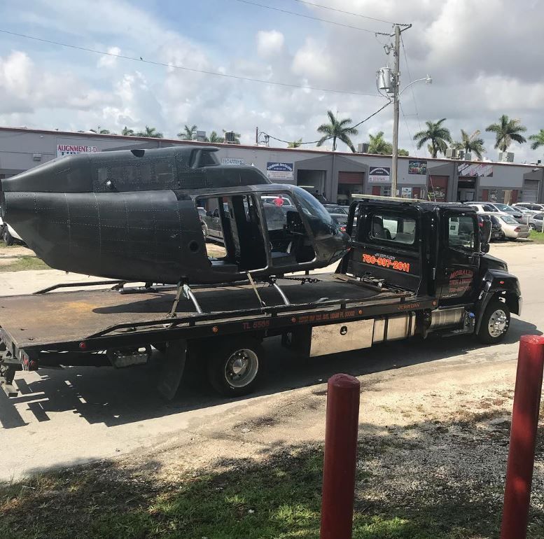 Black helicopter fuselage on a flatbed tow truck. Outside.