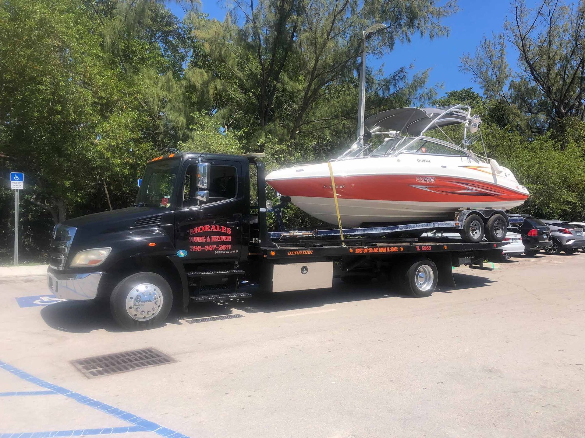 Black tow truck carrying a white and red boat in a parking lot.