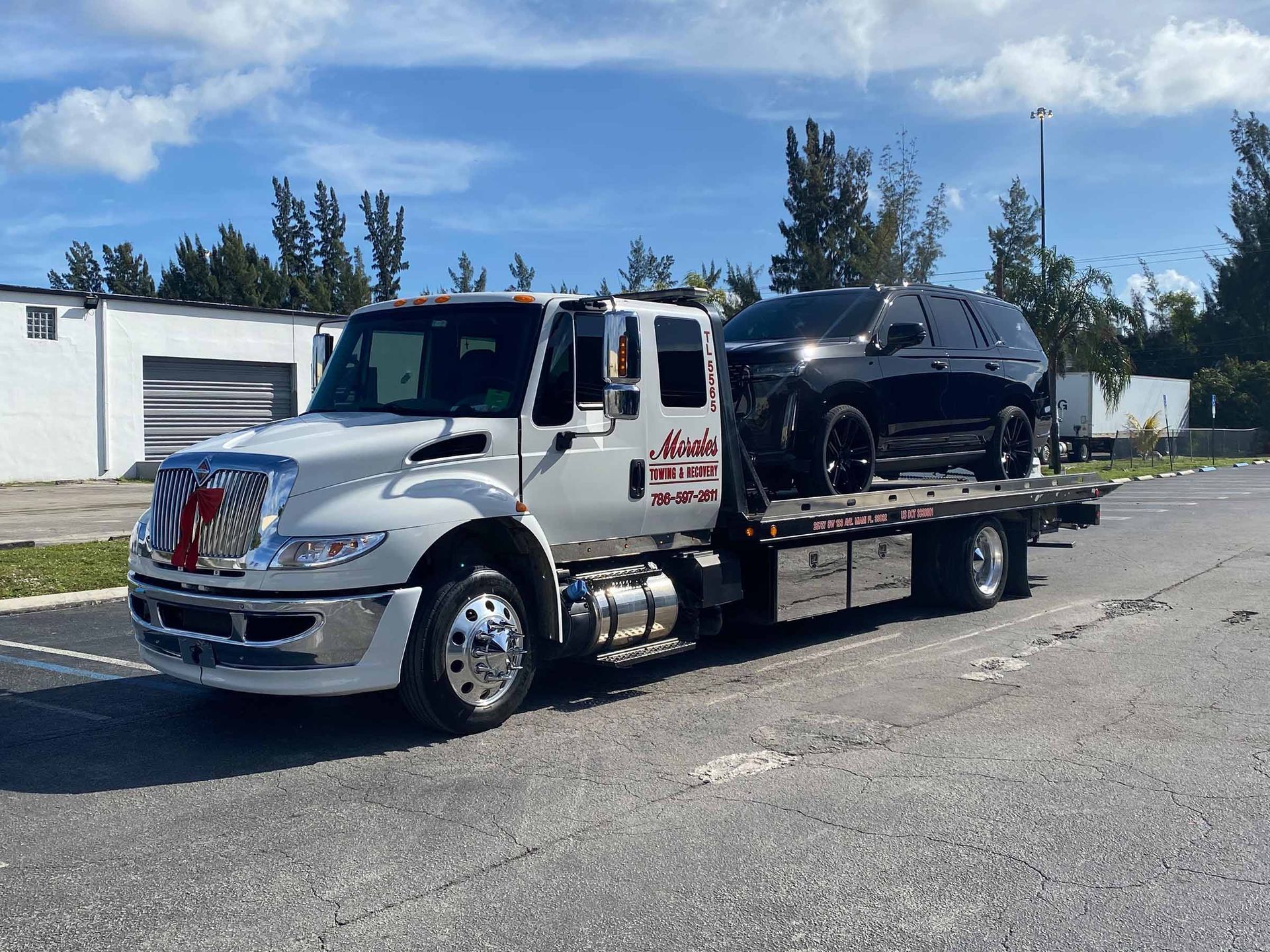White tow truck carrying a black SUV on a sunny day.