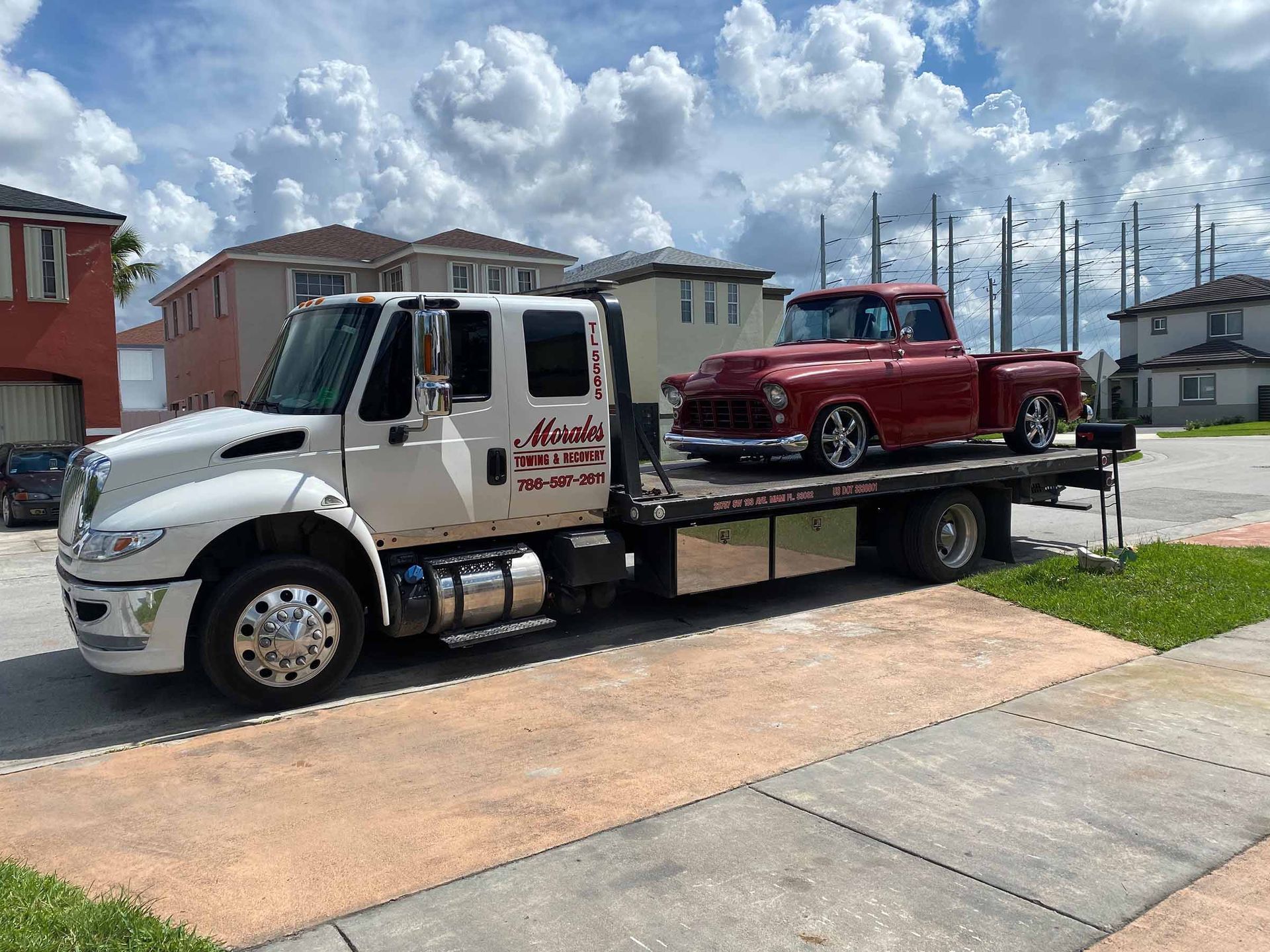 White tow truck carrying a red classic pickup truck on a residential street.