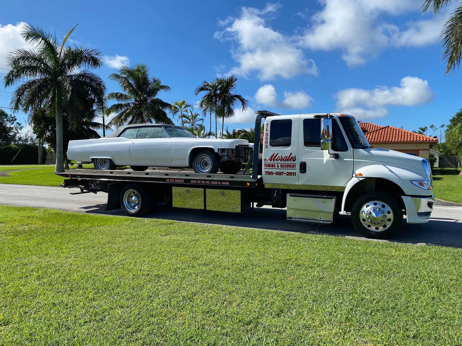 White tow truck carrying a vintage convertible on a sunny day.