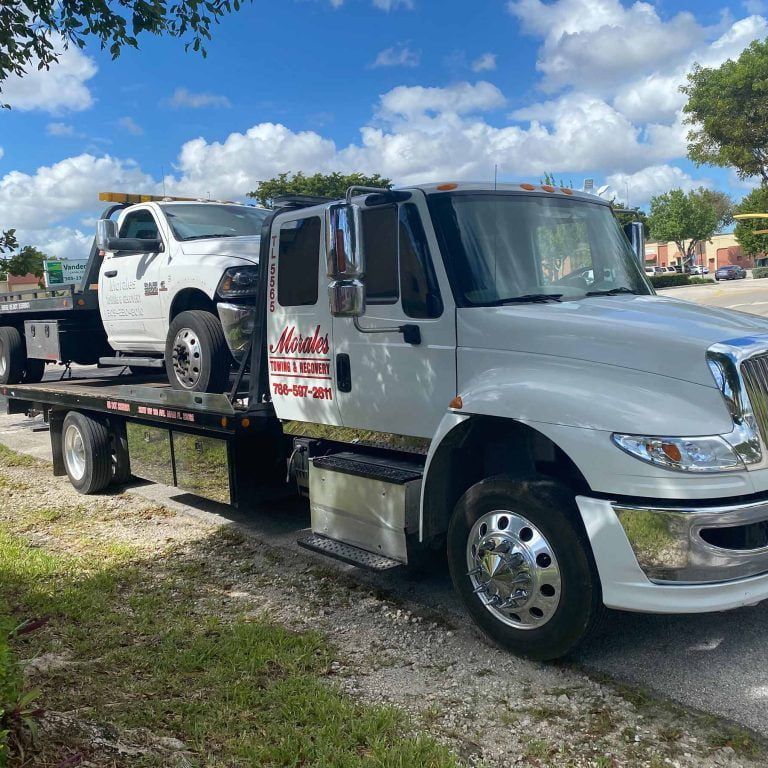 White tow truck hauling a white pickup truck on a sunny day.