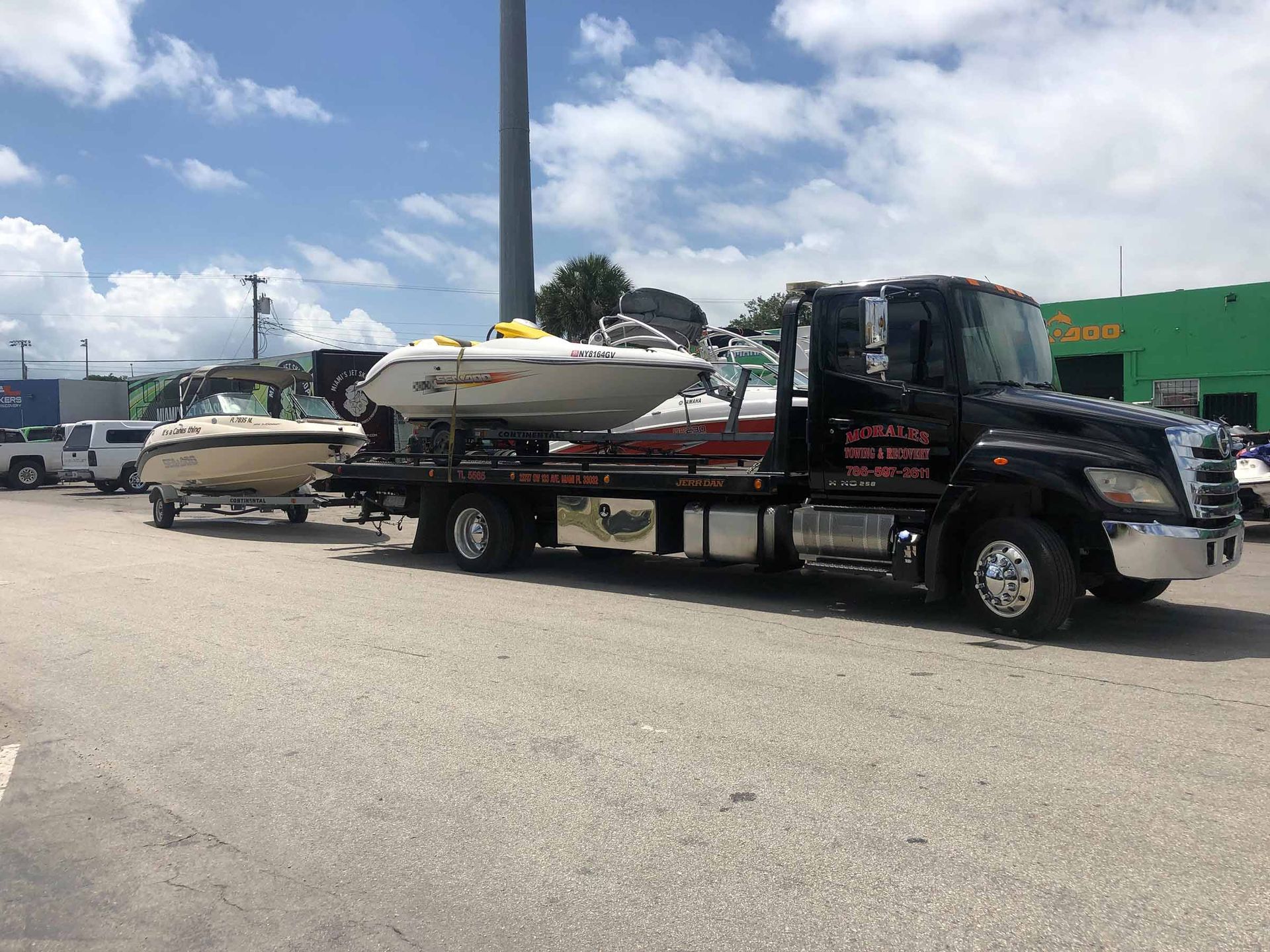 Tow truck carrying two boats on a sunny day.