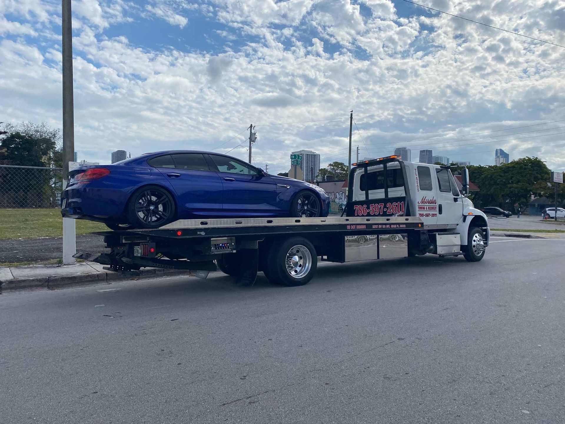 Blue car being towed on a flatbed tow truck on a paved road under a cloudy sky.
