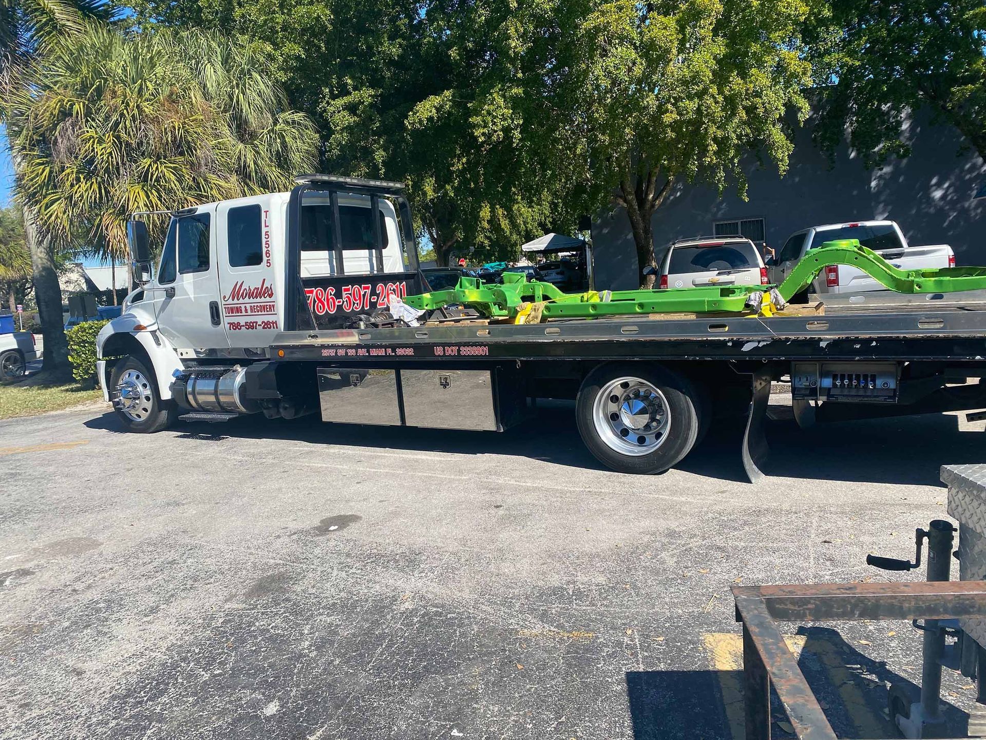 Tow truck with a flatbed in front of a building. It's white and has a green object on the bed.