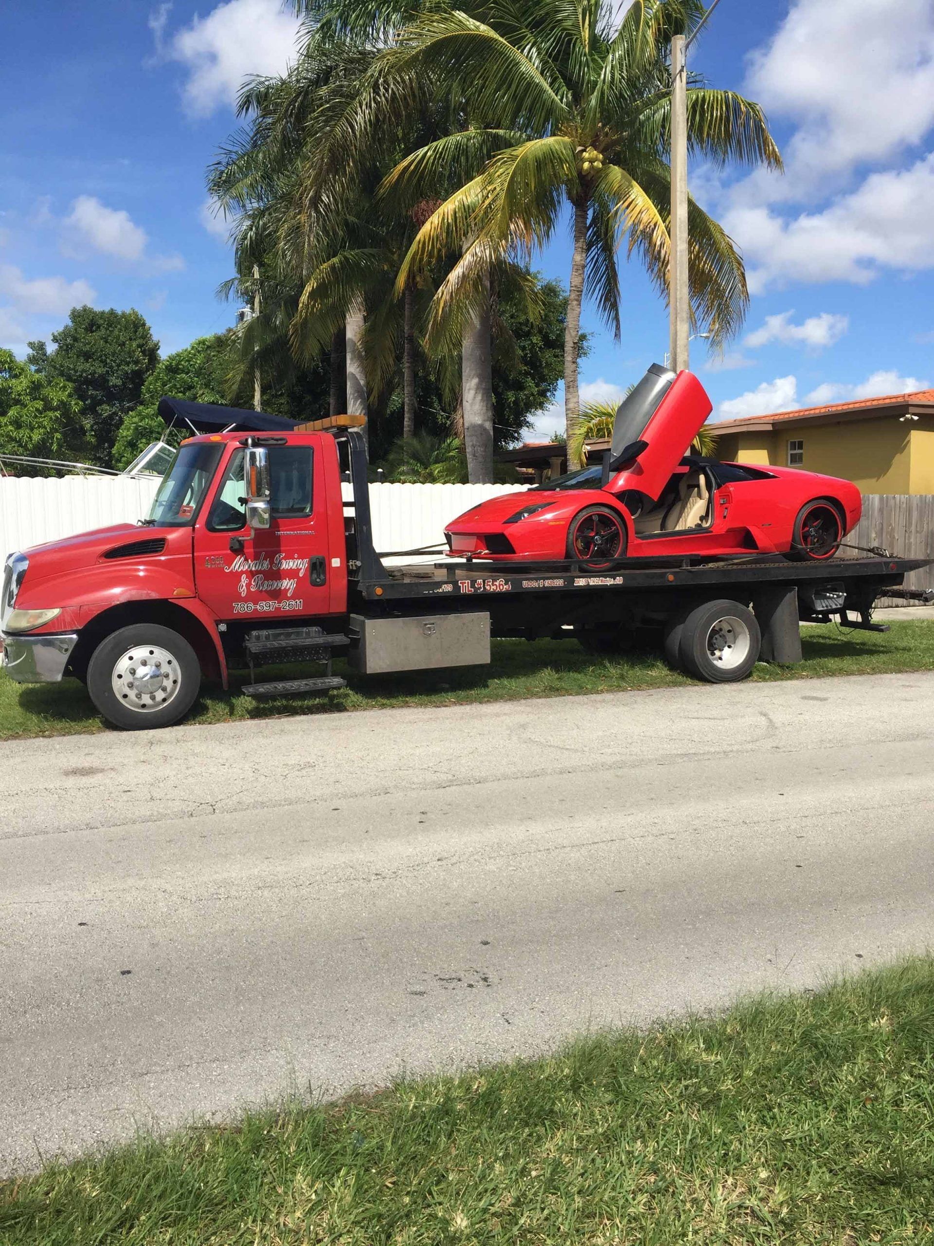 Red tow truck carrying a red sports car with open doors on a residential street.