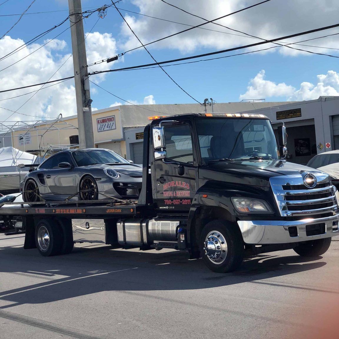 Tow truck hauling a silver sports car on a sunny street.