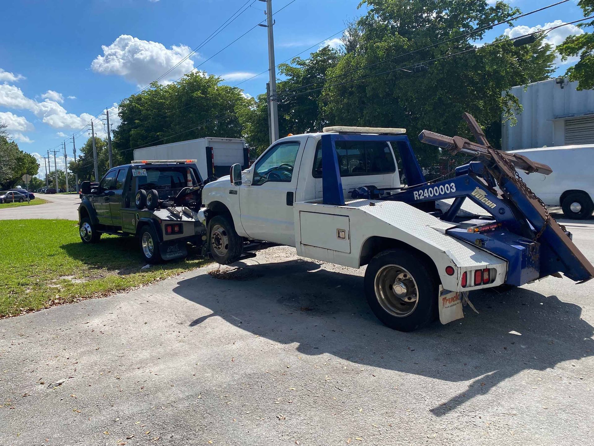 Tow truck hauling a black Jeep on a paved street with trees and buildings in the background.