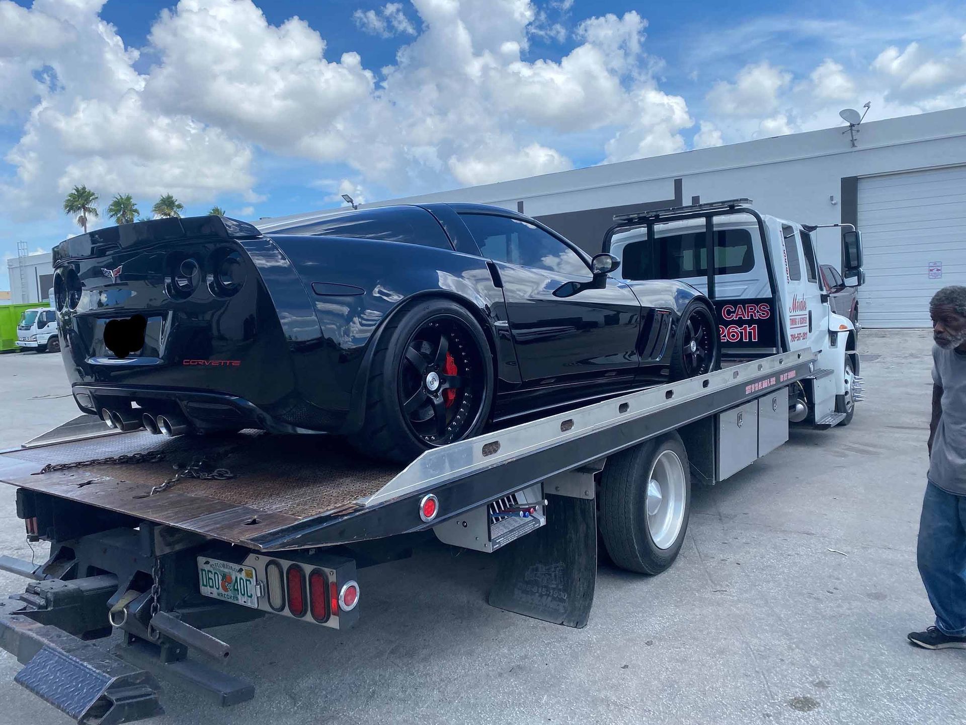 Black Corvette sports car on a flatbed tow truck. Bright, outdoor setting.