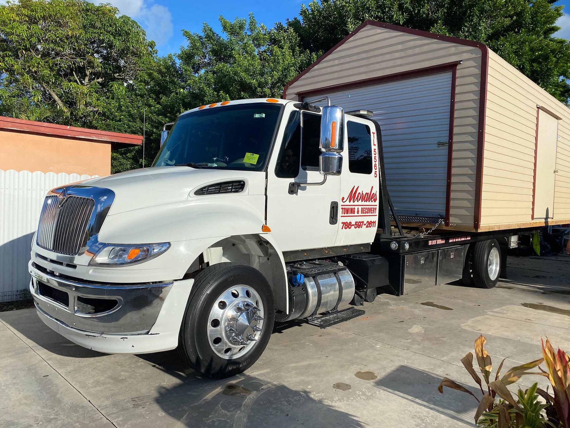 White truck towing a shed on a trailer, parked on concrete. Sunny outdoor setting.