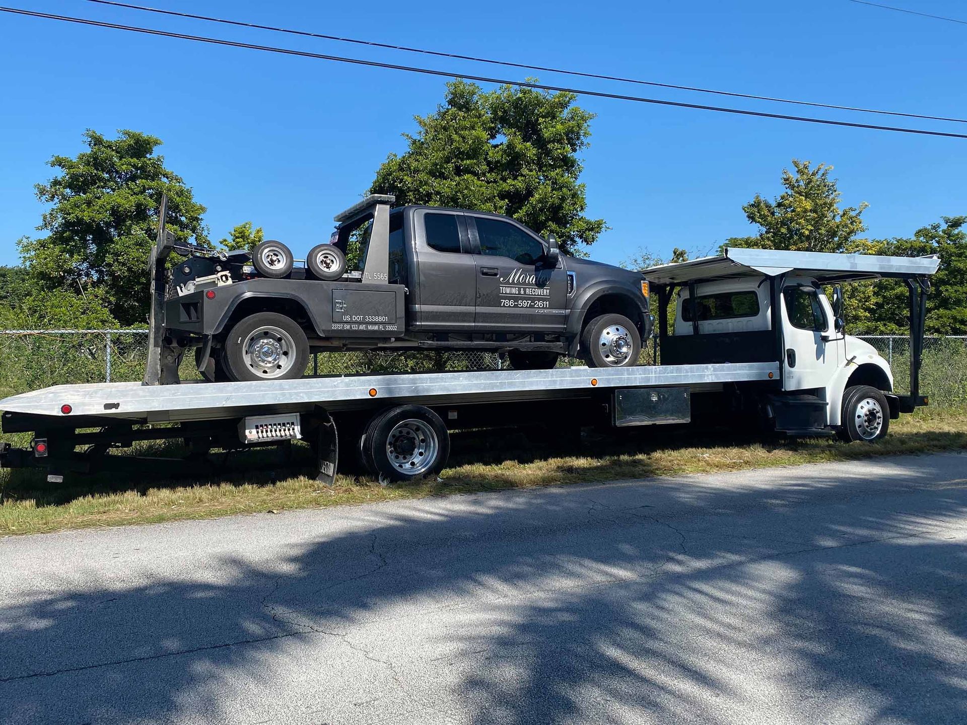 Tow truck carrying a gray pickup truck on a sunny day.