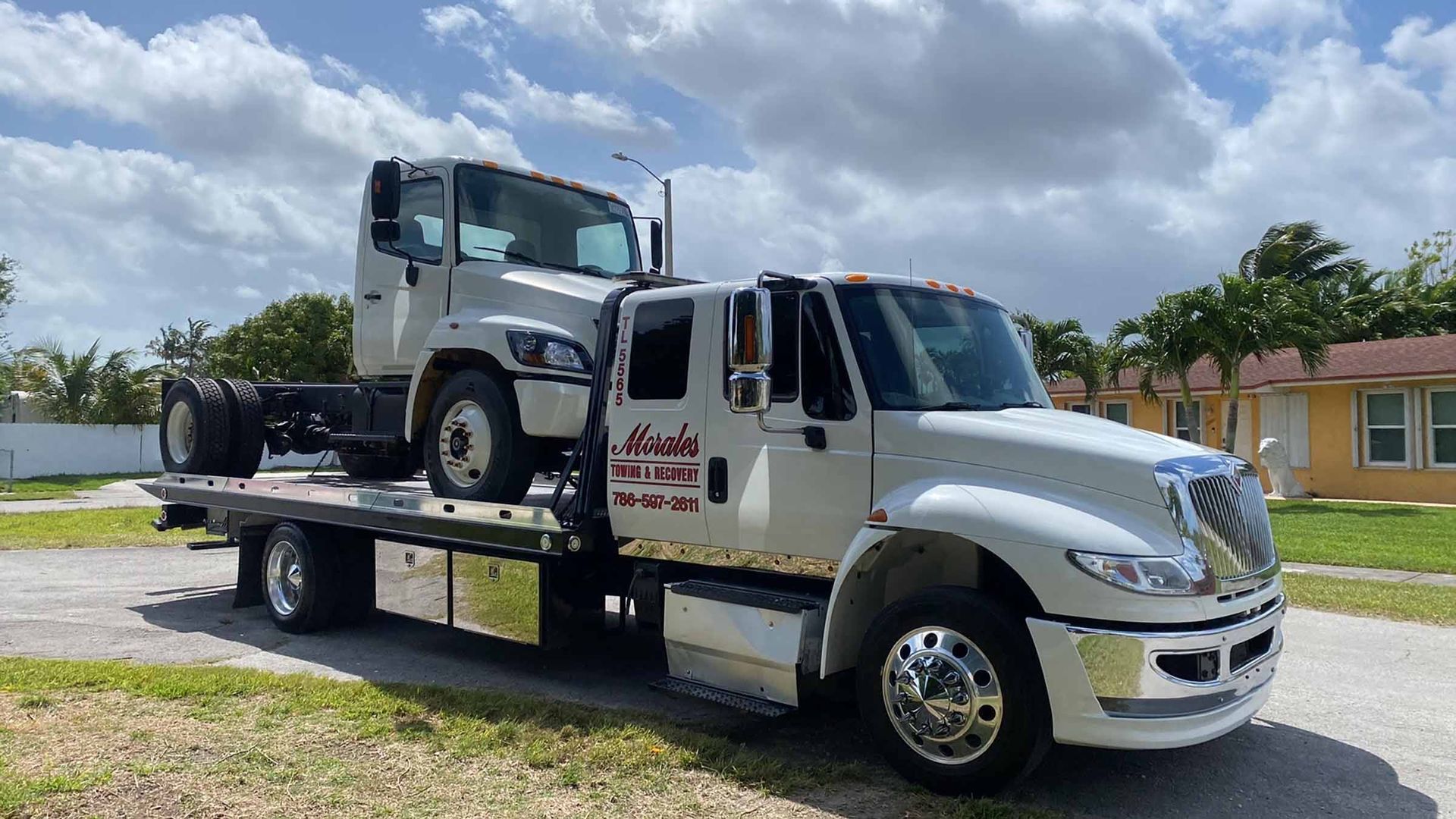 Tow truck carrying a cab over a flatbed on a residential street. The truck is white with chrome accents.