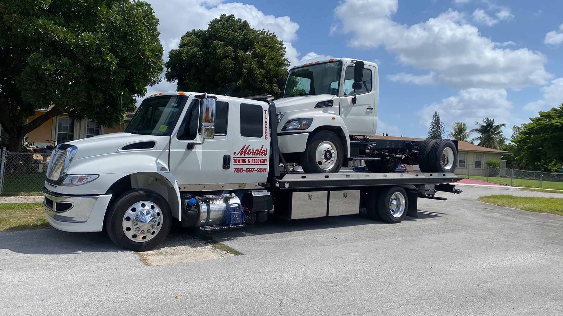 White tow truck hauling a white truck cab on a sunny day.