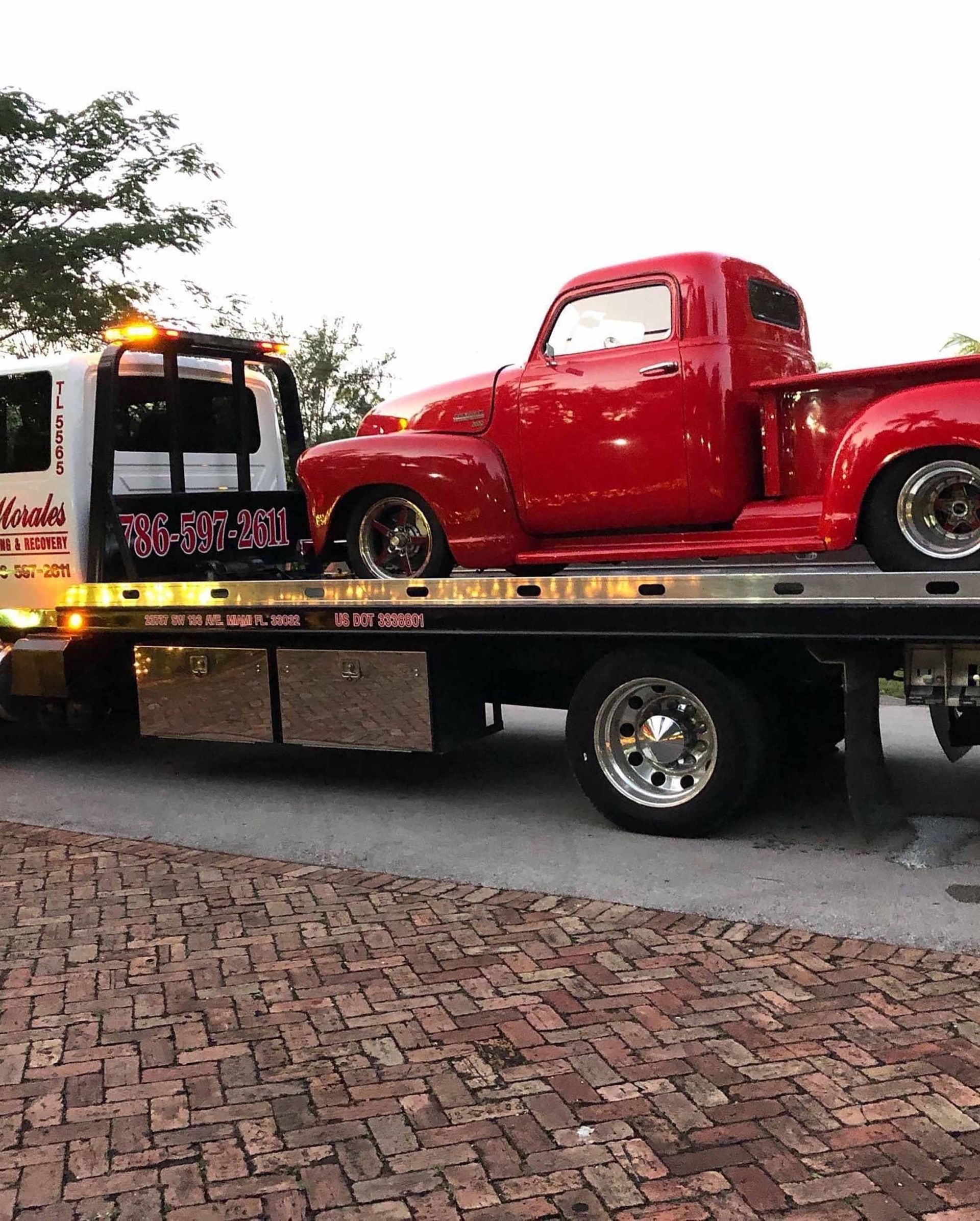 Red vintage pickup truck on a flatbed tow truck on a brick road.