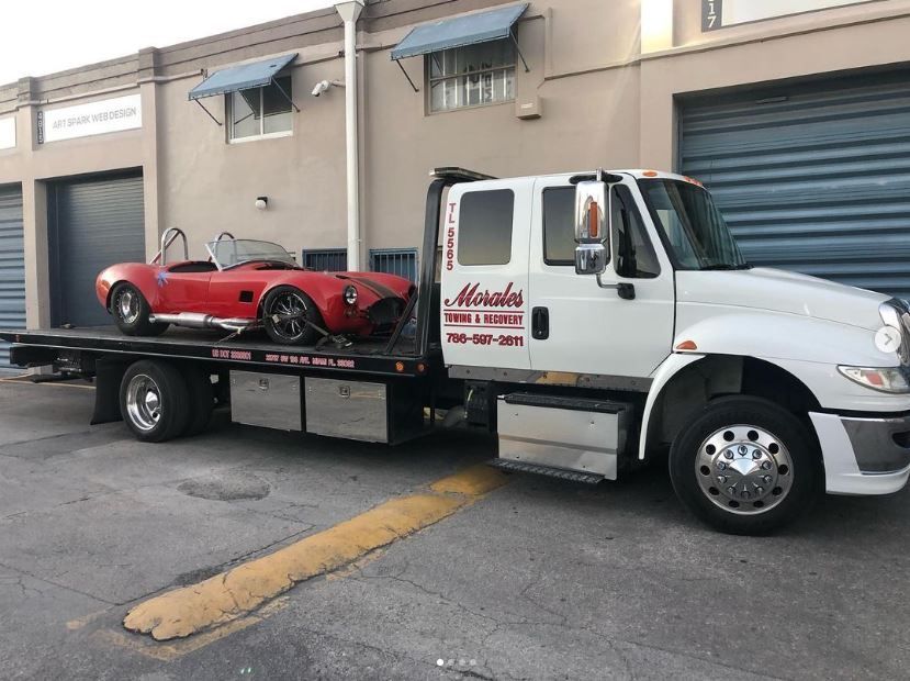 Red sports car on a flatbed tow truck in front of a building.