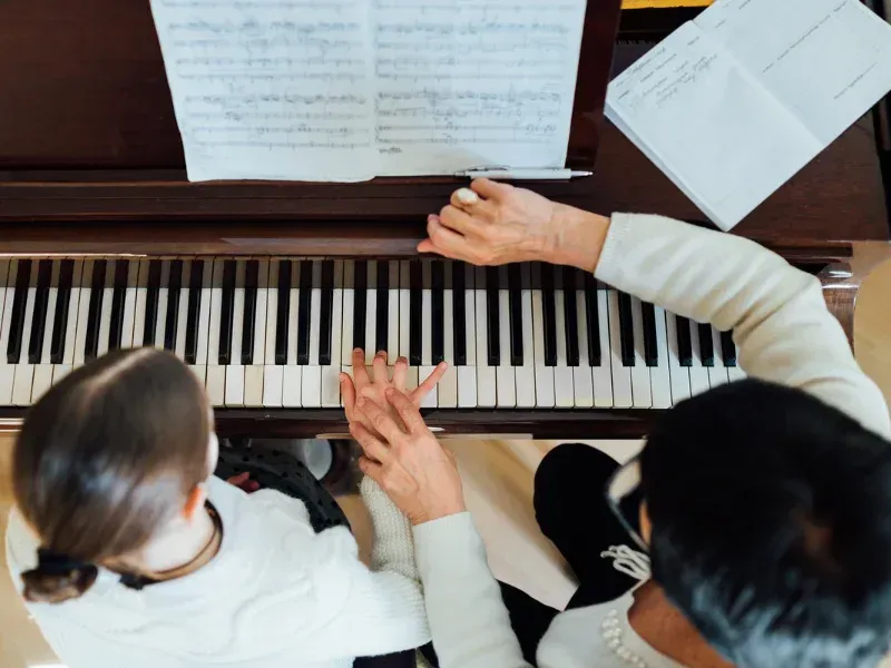 Image of a person learning piano with a teacher.