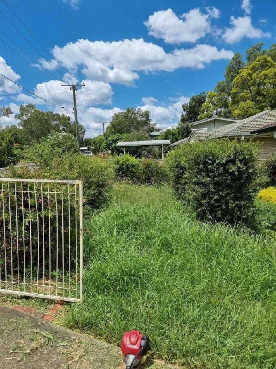 A red lawn mower is sitting in the grass next to a gate.