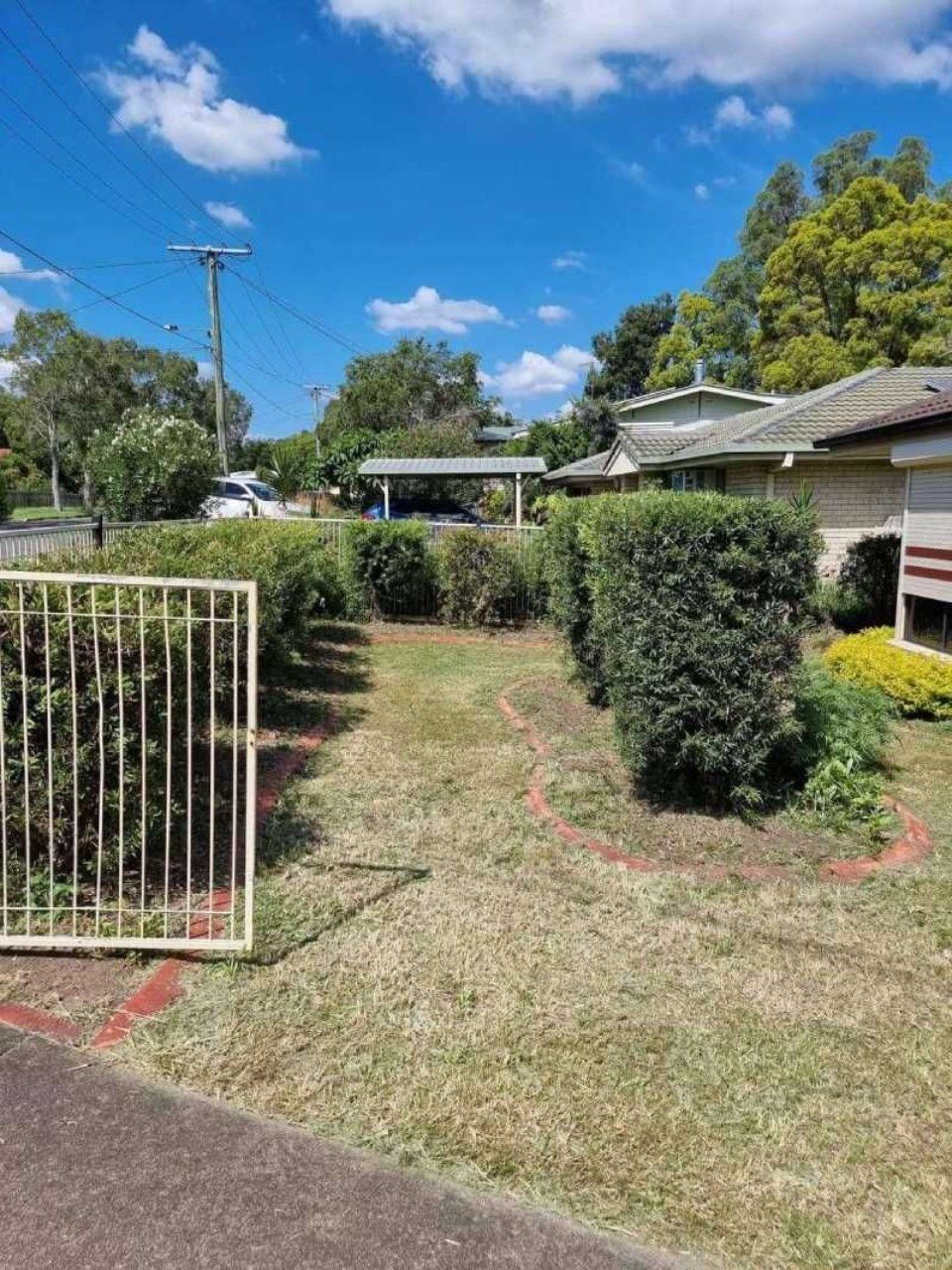 A fence surrounds a lush green yard with a house in the background.