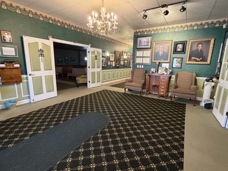 Funeral home interior with green walls, patterned carpet, portraits, and seating.