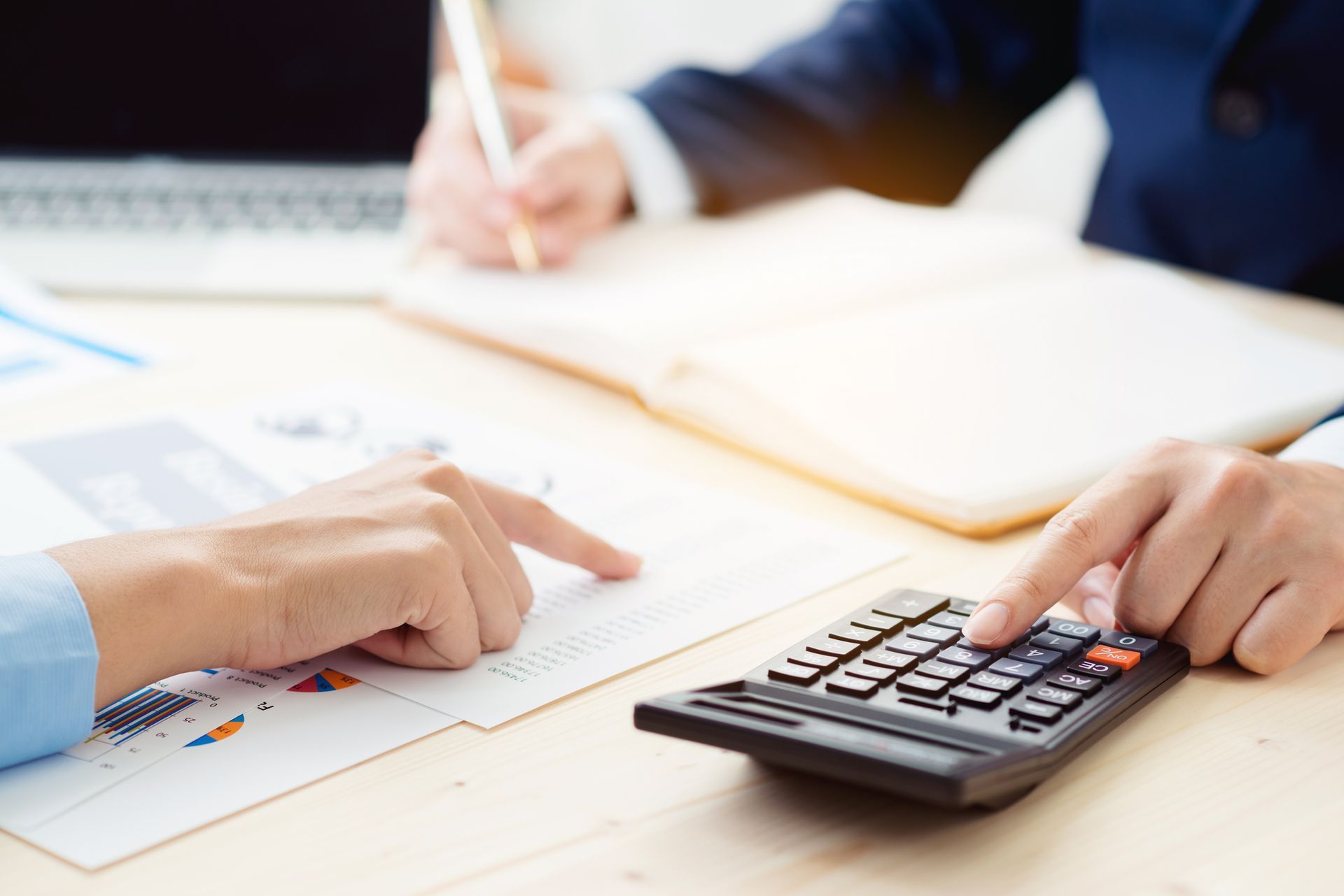 Hands pointing at documents, using calculator, and writing in a notebook at a desk.