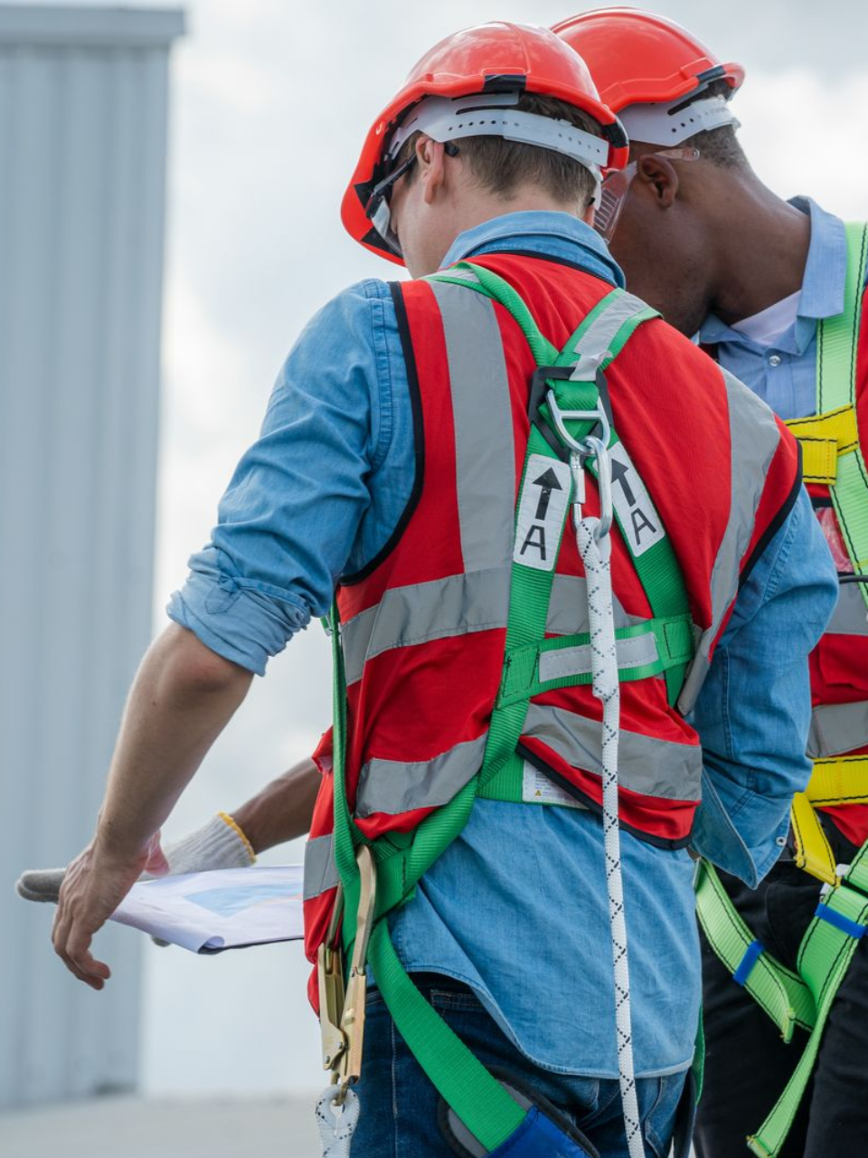 Two roofers, wearing safety gear and hard hats, reviewing a project's scope of work outdoors.