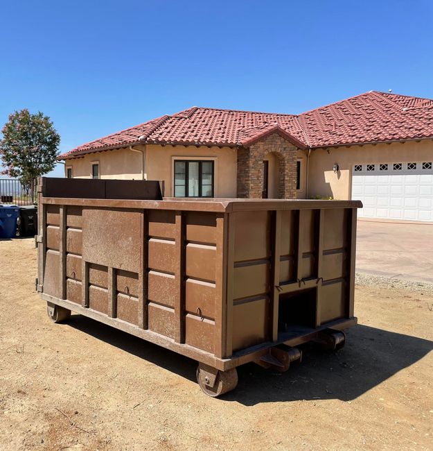 A large black dumpster is parked in front of a row of houses