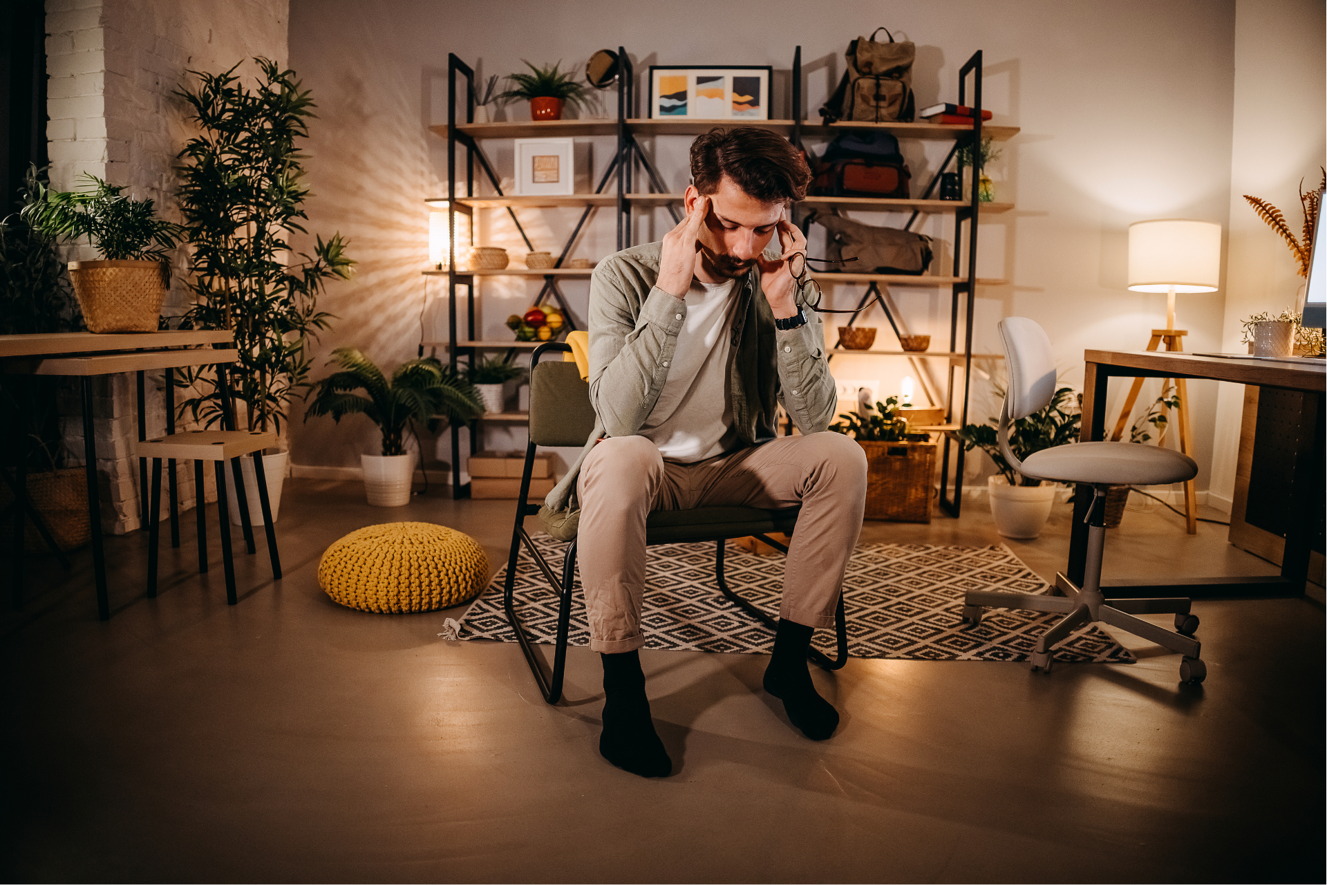 A man is sitting in a chair in a living room covering his ears with his hands.