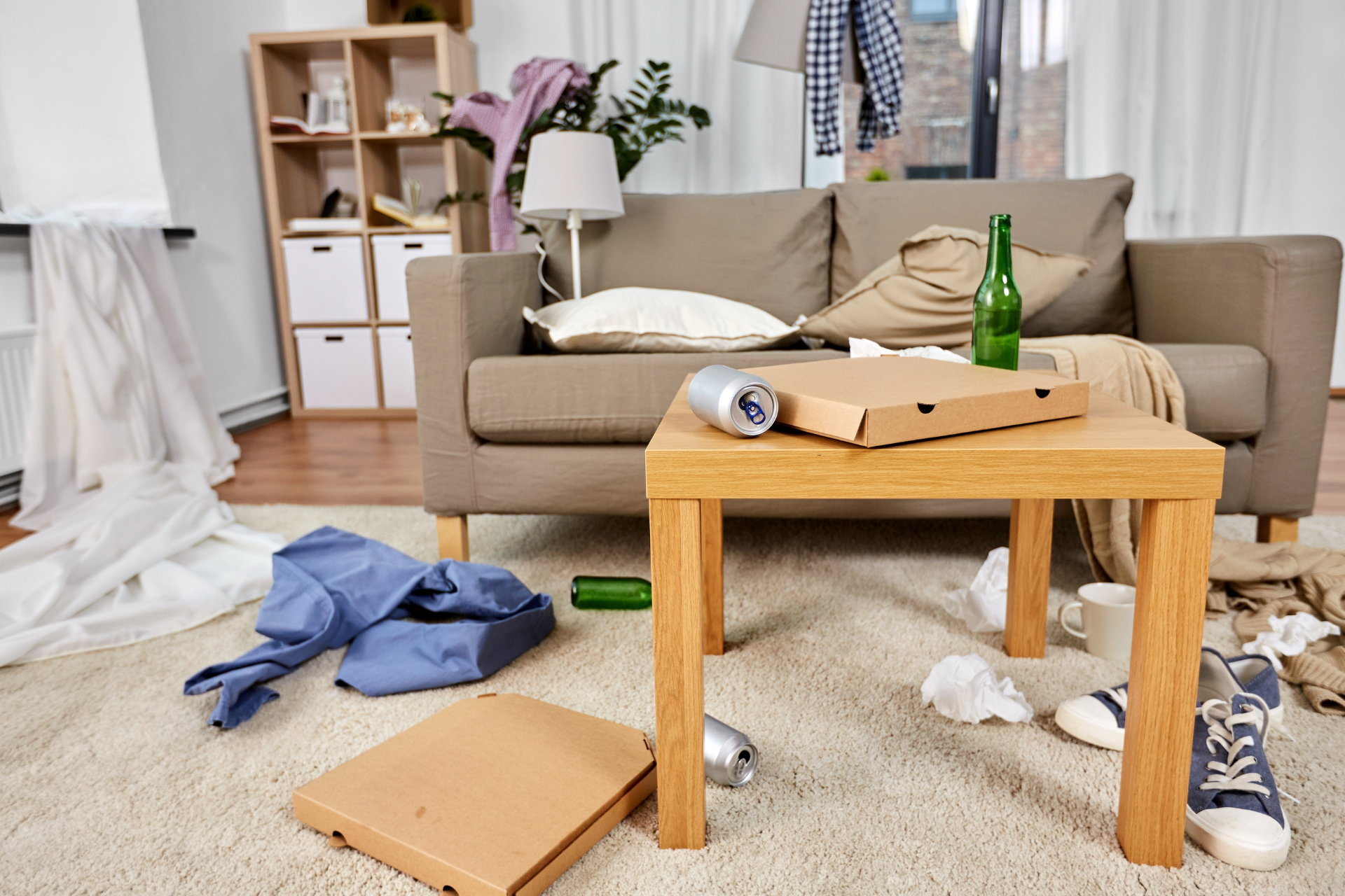 A messy living room with a couch , table , and pizza boxes on the floor.